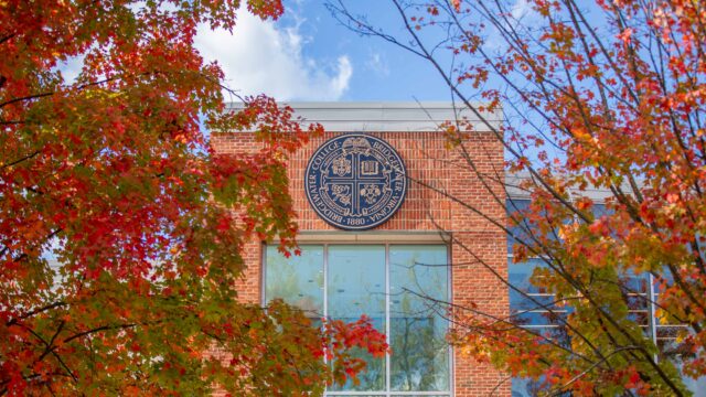 The exterior of the Forrer Learning Commons that shows the Bridgewater College seal. Trees with fall leaves surround it.