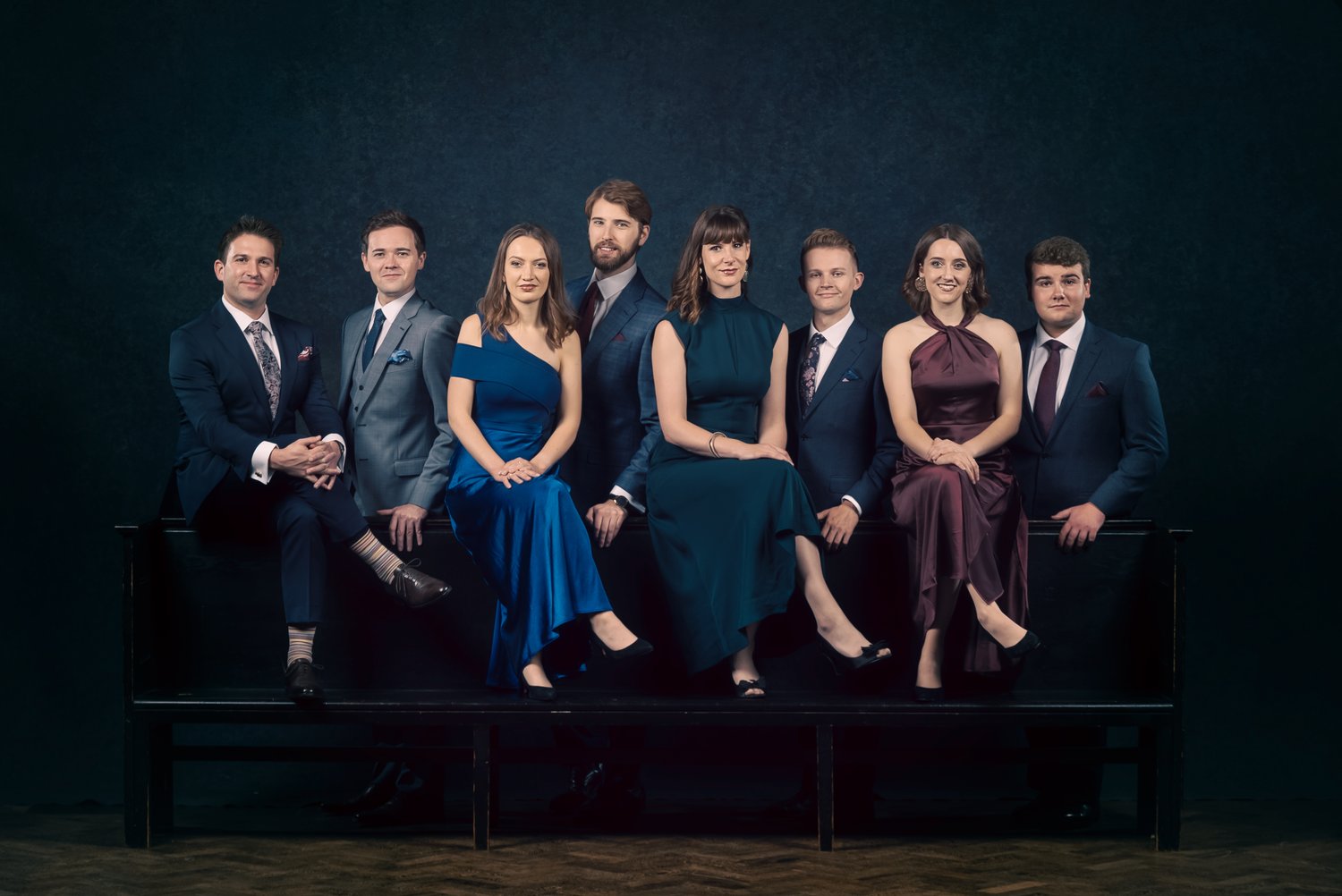 A group of 8 men and women sitting in formal wear.