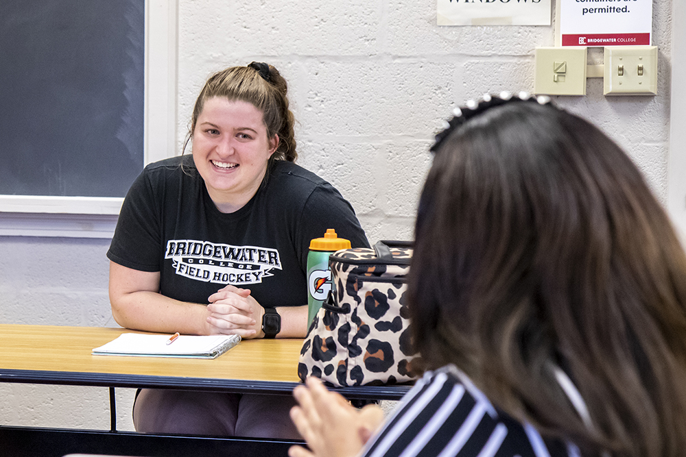 Student smiling in class with professor sitting across from her
