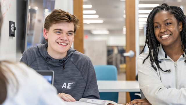 Two students sitting next to each other smiling in human resources class