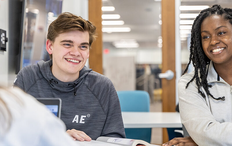 Two students sitting next to each other smiling in human resources class