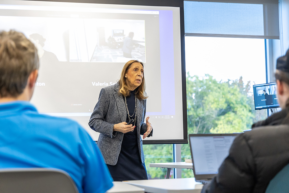 Professor standing at the front of the class with projector screen behind her