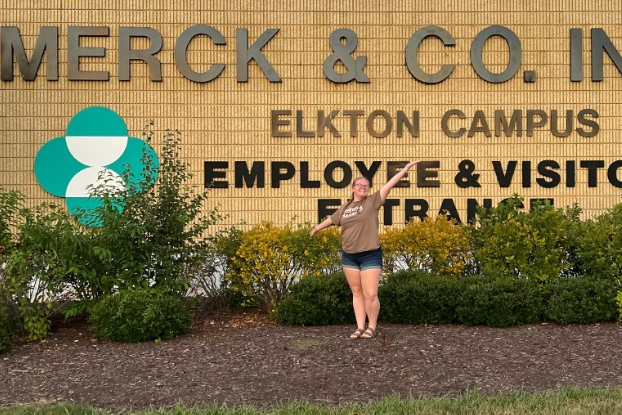 Student posing in front of large brick sign that reads Merck & Co. Inc. Elkton Campus. Employee & Visitor Entrance.