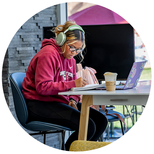 Student wearing green headphones sitting at table writing in a notebook