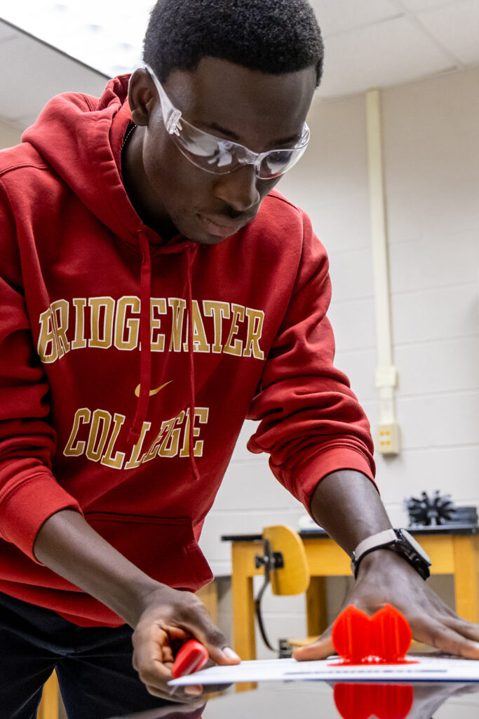 Student in crimson Bridgewater College sweatshirt working with 3-D printed item