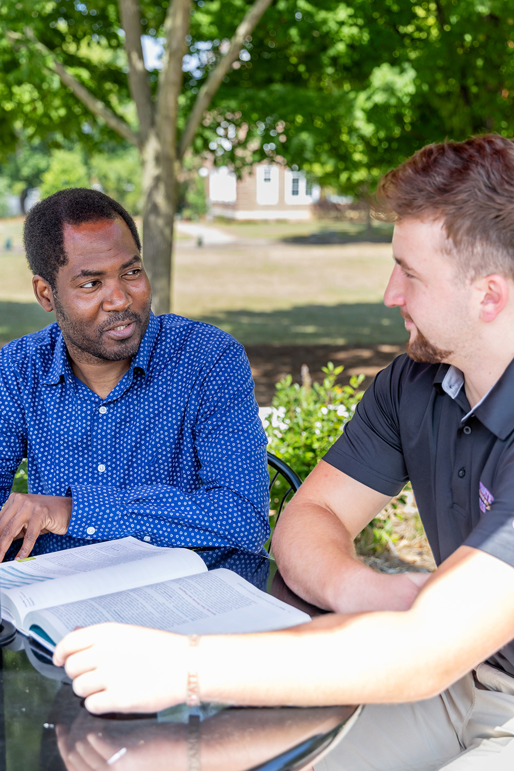 Professor speaking with student with book open on the table in front of them