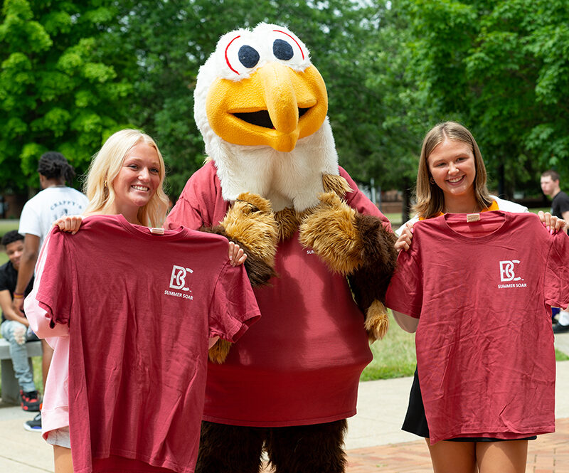 Students posing with mascot Ernie holding crimson t-shirts for summer soar orientation
