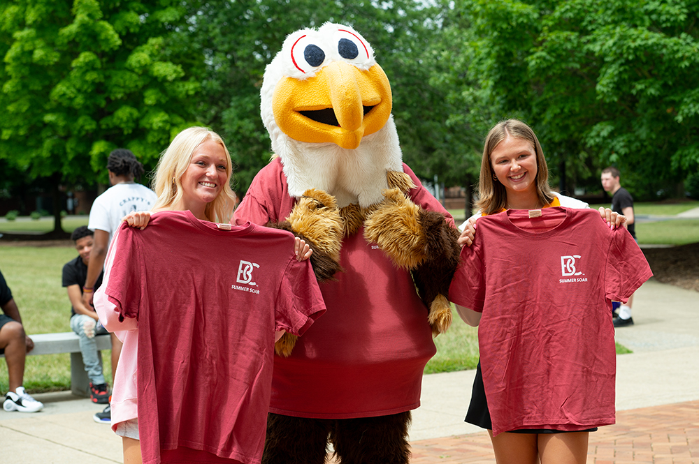 Students posing with mascot Ernie holding crimson t-shirts for summer soar orientation