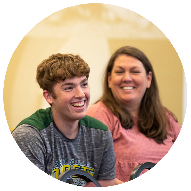 Student smiling in the foreground with mom smiling in the background