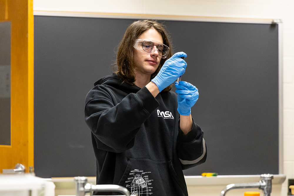 Student wearing NASA hoodie and blue gloves in forensics lab