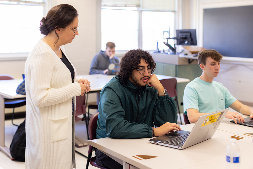 Professor looking over students shoulder at laptop in class 