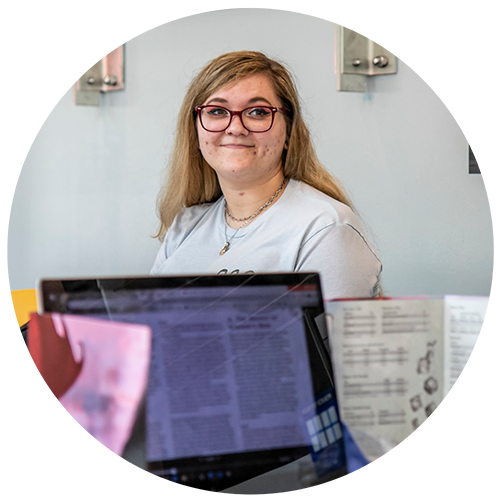 Student with glasses smiling with laptop in the foreground