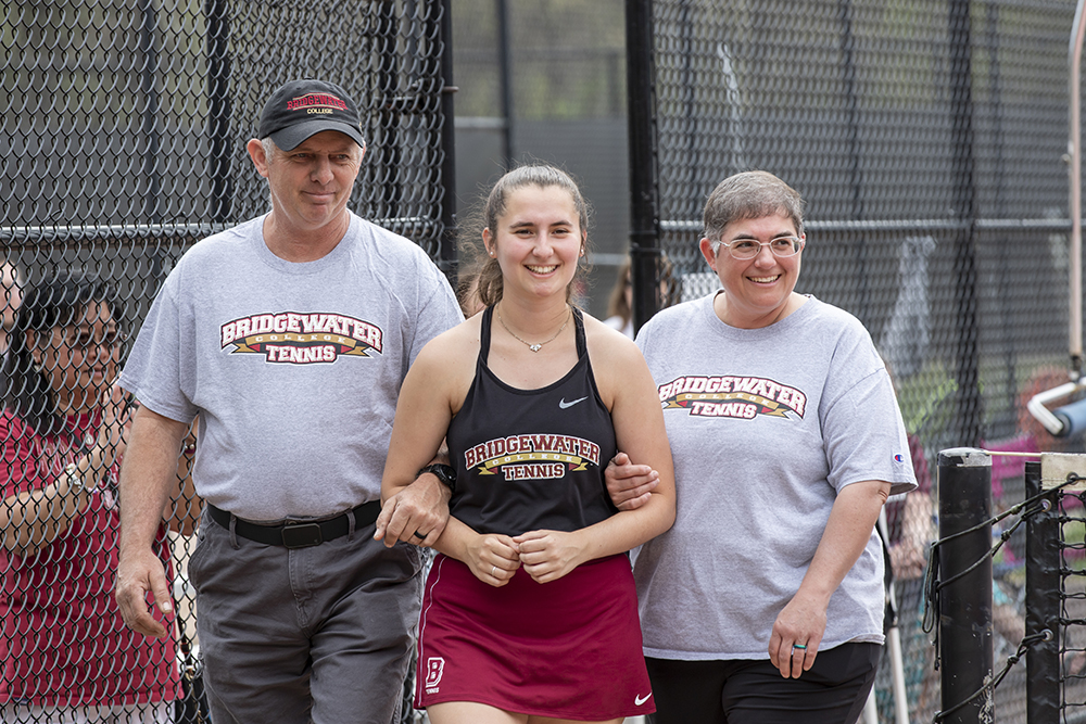 Father and mother linking arms with daughter on senior day