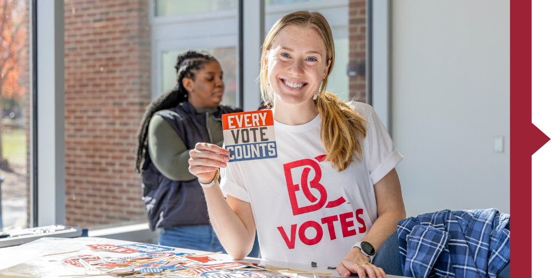 A female student wearing a B-C votes shirt and holding a sticker that says every vote counts