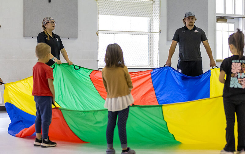 Students playing parrachute games with young children