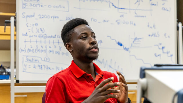 Student in red polo sitting in front of a white board with formulas on it