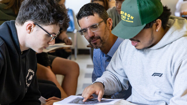 Professor meeting with two students as they look at a picture on the desk
