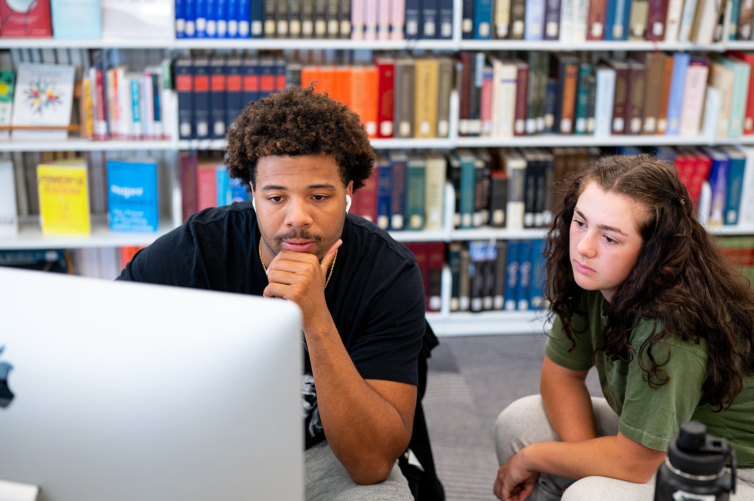 Students looking at a computer screen in the F-L-C with a bookshelf behind them