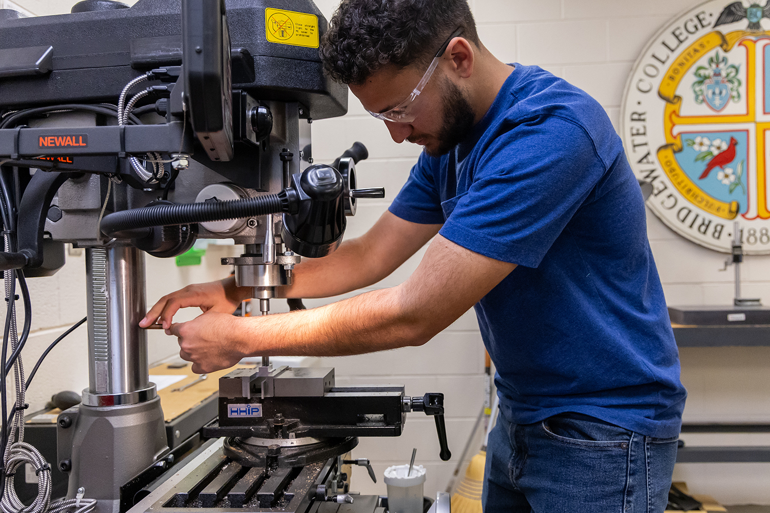 Student wearing blue shirt standing in front of drilling equipment in engineering lab