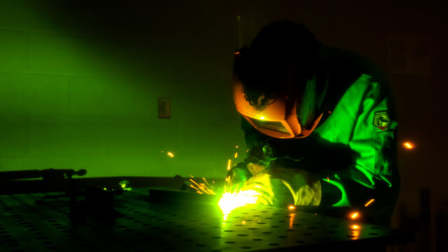 Person welding in the dark with a green glow coming from the welder