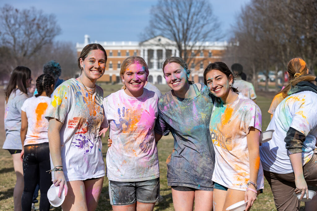 Four students covered in bright powder smiling during Holi event