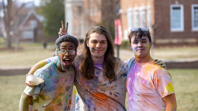 Three students covered in bright powder smiling during Holi event