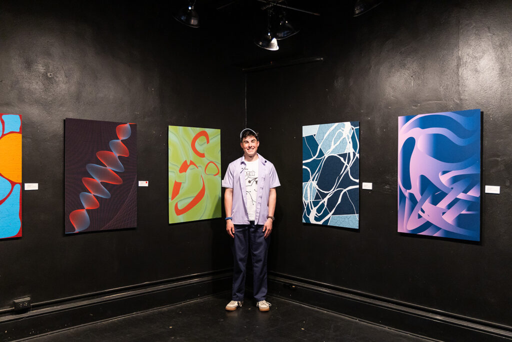 Student posing with his artwork of bright paintings for his senior thesis project