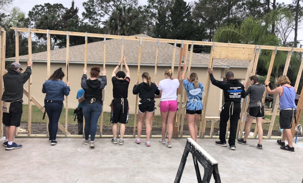 Students lifting framing for a house into place