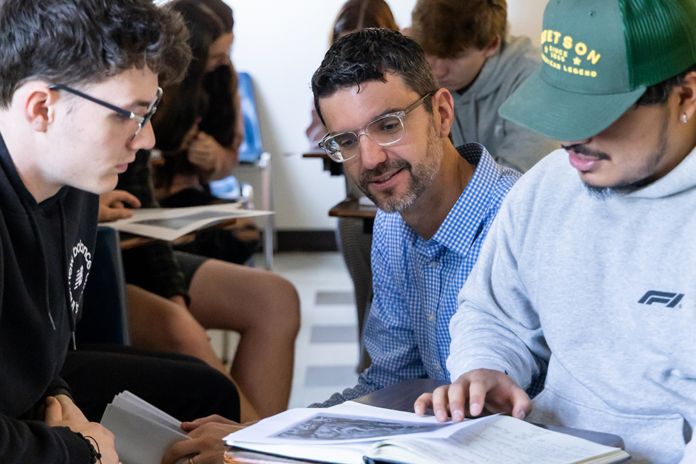 Professor meeting with two students as they look at a picture on the desk