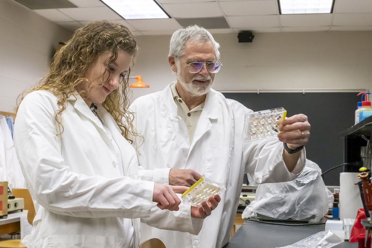 Dr. Baron and a Bridgewater College biology degree student collaborating on lab research in white lab coats.