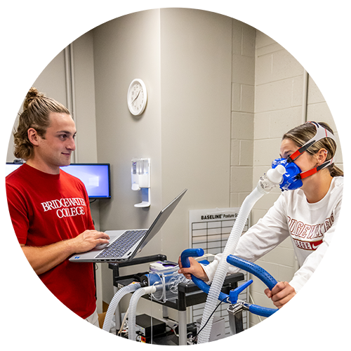 Health and exercise student at Bridgewater college working on research project with a student on a bike hooked up to equipment to measure fatigue