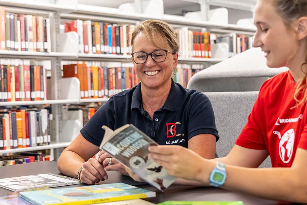Dr. Martin smiling while sitting with student holding a book and discussing a research project