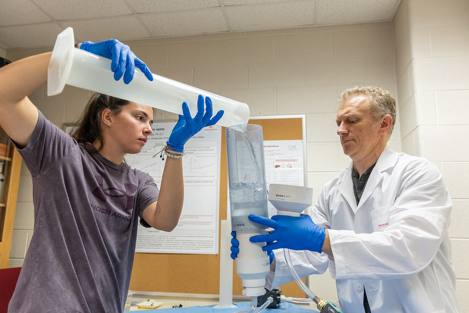 Student pouring a liquid into a tube a professor is holding for a summer research project