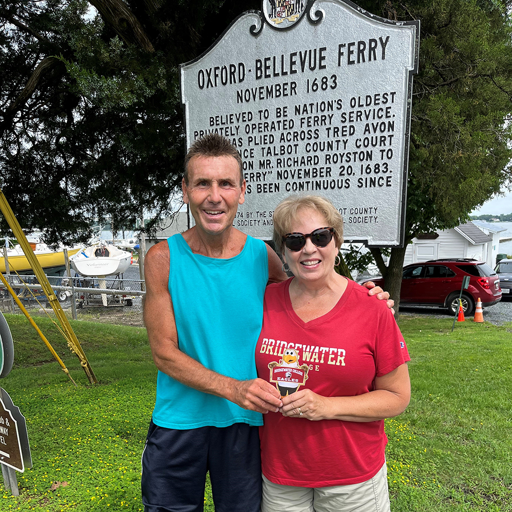 Man and woman holding Flat Ernie in front of historical sign for Oxford Bellevue Ferry. 