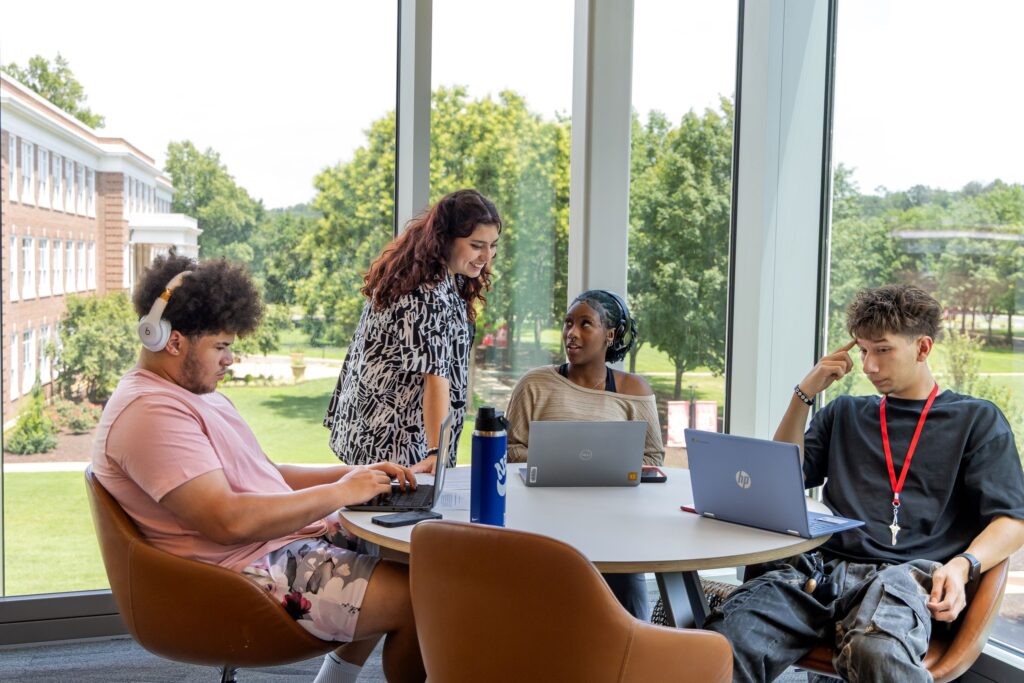 Four students hard at work at a table by large windows