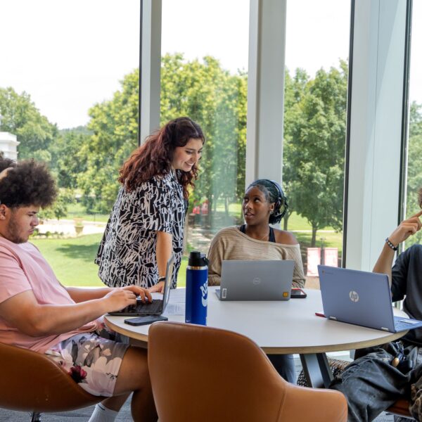 Four students hard at work at a table by large windows