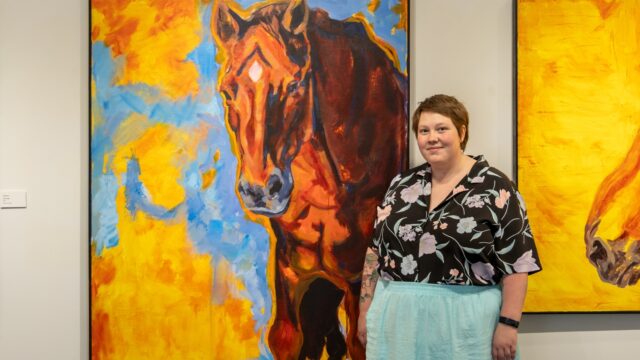 Artist stands proudly in front of a painting of a horse that is larger than the artist.