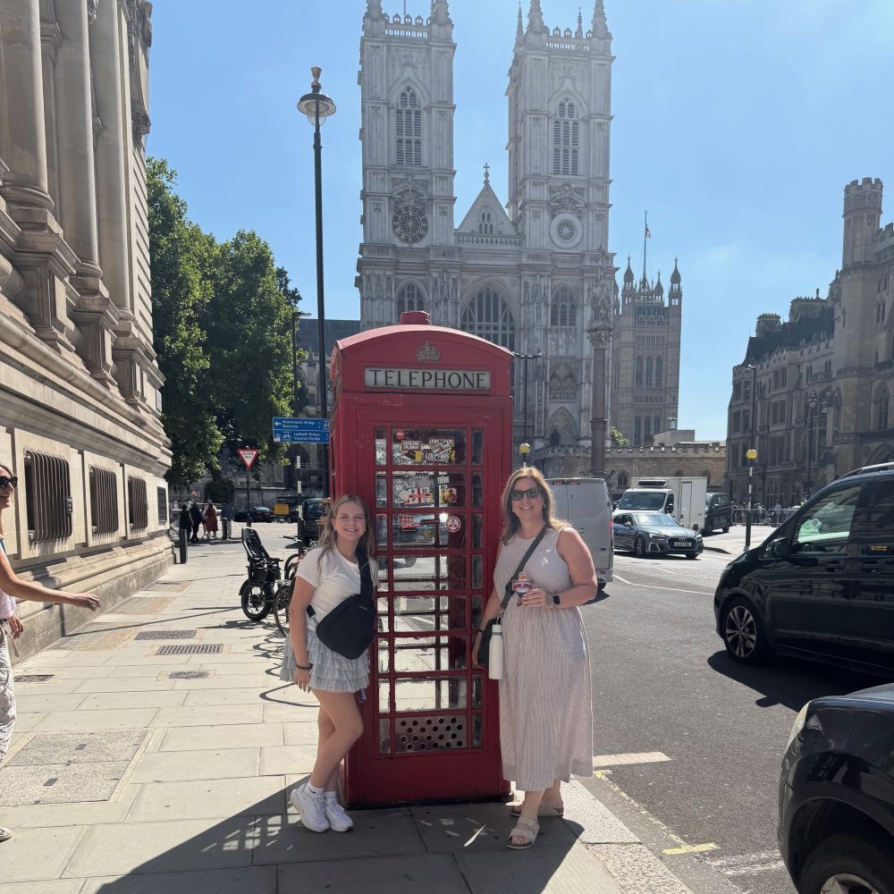 L Bissett and her daughter stand with flat Ernie beside a phone booth in front of a cathedral in London