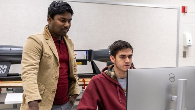 Student working at a computer with a professor looking at the screen