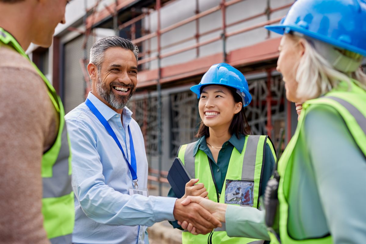 A man in business casual greets a group of construction workers like old friends