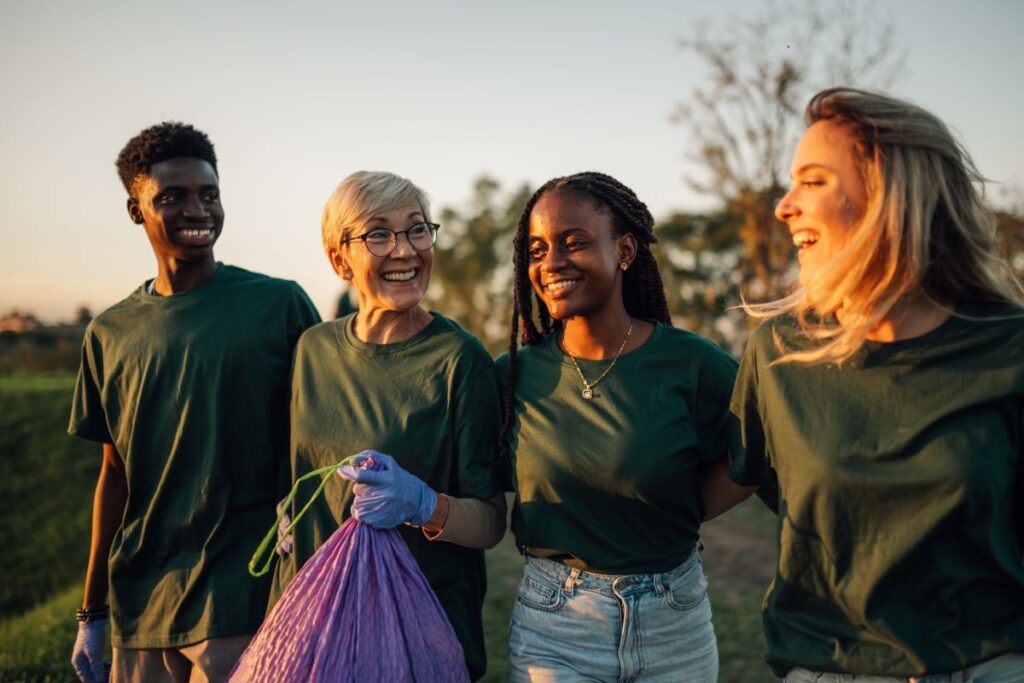 A group of smiling friends walk together in matching shirts, picking up trash