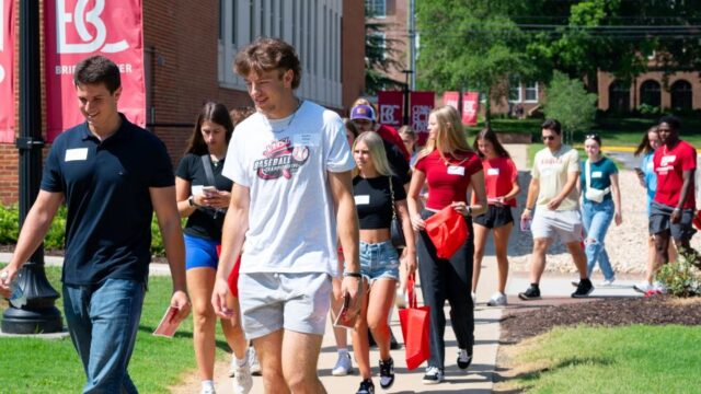 New students walk in pairs down a sunny sidewalk, talking with each other