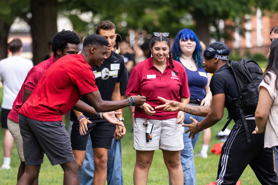 Two students play rock paper scissors in a circle of cheering peers