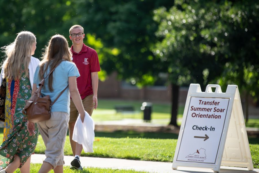 Visitors walk toward a transfer orientation sign. They are greeted by a cheery student