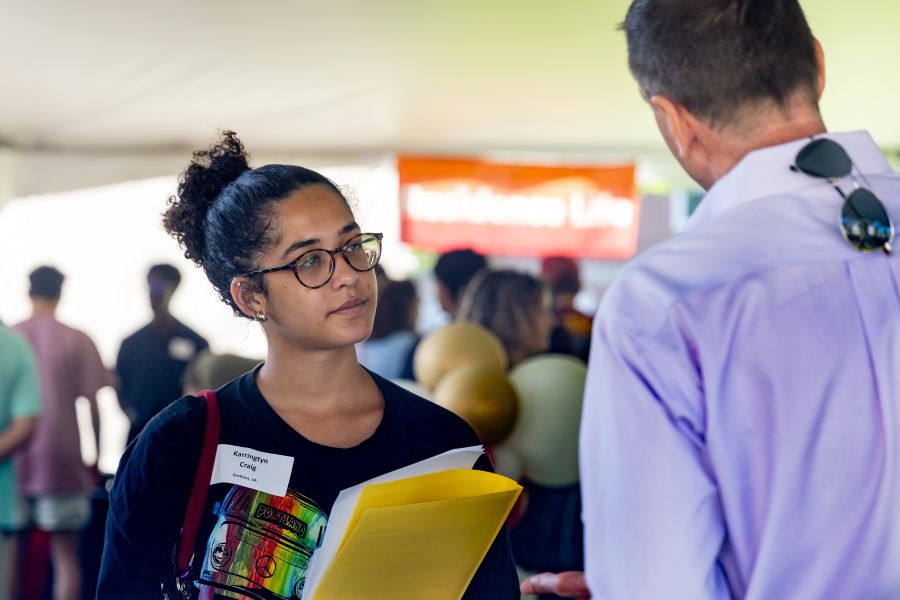 A student and professor chat under a large tent
