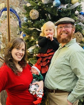The Oates family stand in front of a Christmas tree. Kristina holds baby Declán
