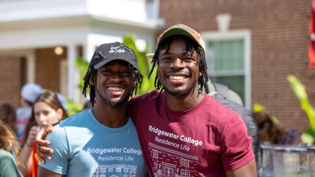 Two students in hats smiling and reaching their arms around each others' shoulders