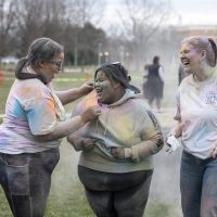 students laugh together on the mall during Holi holiday event. the students are covered in powder paint