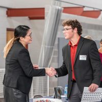 A student in a suit shakes hands with a recruiter