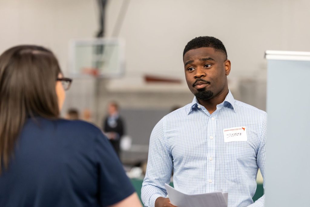 A male student in professional attire talks to a recruiter